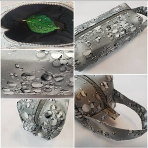 May include: A gray zippered pouch with a white and gray bubble pattern. The pouch has a zipper closure and a handle. The pouch is open to reveal a black interior.