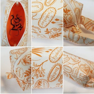 May include: A white fabric cosmetic bag with an orange zipper and a repeating pattern of orange botanical illustrations and text. The text includes the names of plants like Maidenhair, Bird's Eye, Angelica, Yarrow, Foxgloves, and Crow's.