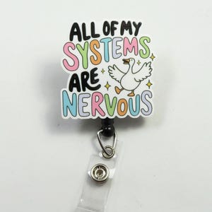 Op de afbeelding: Een witte badgehouder met een kleurrijke afbeelding waarop staat "All of my systems are nervous" met een cartoon-gans. De badgehouder heeft een zwart intrekbaar koord.