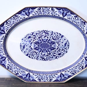 May include: An octagonal serving platter with a white base and a dark blue floral pattern. The design features a central oval medallion filled with intricate botanical motifs, surrounded by a decorative border with a gold-toned rim edge.