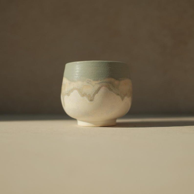 Op de afbeelding: Een witte keramische beker met een lichtblauwe glazuur. De glazuur heeft een druppel-effect, waardoor een uniek patroon ontstaat.