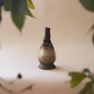 Op de afbeelding: Een bruine en beige keramische matcha-garde met een zwart touwtje om de bovenkant gebonden. De garde staat op een wit oppervlak.