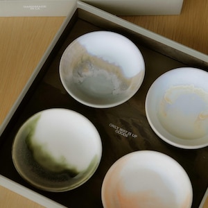 May include: Four small, round ceramic bowls with unique color gradients, presented in a rectangular box. The bowls feature white, green, peach, and gray tones. The box has the text "ONLY WAY IS UP GOODS" and "HANDMADE IN LA".