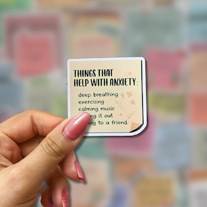 May include: A square sticker with the text "THINGS THAT HELP WITH ANXIETY:" and a list of coping mechanisms. The sticker is held by a hand with pink nail polish, with a colorful background of other stickers.