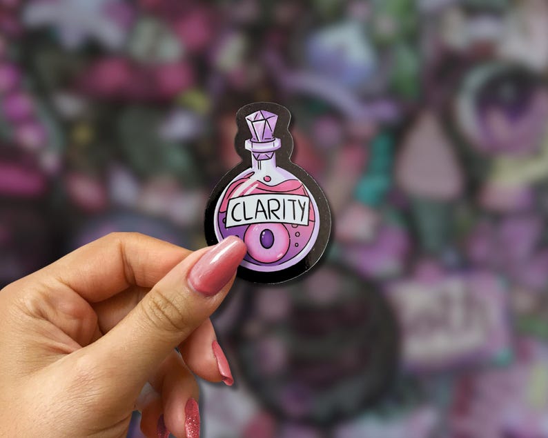 May include: A sticker featuring a potion bottle design with the word "CLARITY" in a black border. The bottle contains a pink liquid and a purple eye-shaped object. The bottle has a purple gem-like stopper.