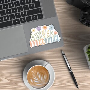 May include: A sticker with a floral design and the word "mama" in pastel colors. The sticker is on a laptop.