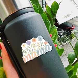 May include: A black stainless steel water bottle with a floral sticker that says "mama" in a light blue, pink, and white font.