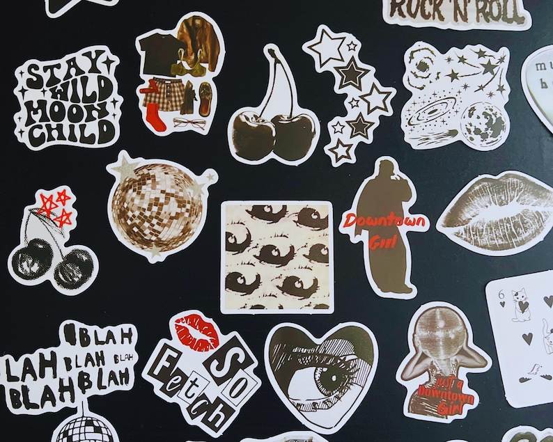 May include: A collection of various stickers with white borders on a black background. Designs include cherries, stars, a disco ball, lips, and text such as "Stay Wild Moon Child" and "So Fetch". The stickers are in shades of brown, white, and red.