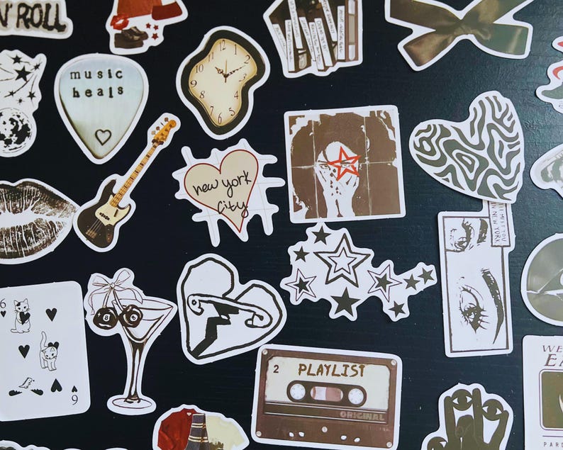May include: A collection of assorted stickers with various designs. Includes a guitar, a heart with "new york city" text, a cassette tape labeled "PLAYLIST", a clock, and a lips design. The stickers are in shades of brown, white, and black.