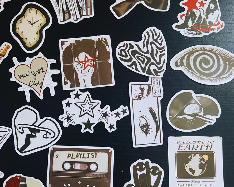 May include: A collection of various stickers with diverse designs. Includes a melting clock, a heart-shaped sticker with "new york city" text, a cassette tape labeled "PLAYLIST", and a sticker with the text "WELCOME TO EARTH". The stickers are in shades of brown, white, and black.