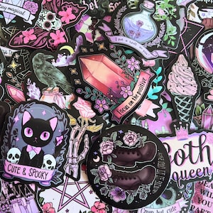 May include: A collection of colorful stickers with a gothic theme. Designs include a black cat with skulls, a crystal, a raven, a potion bottle, and the text "Cute & Spooky" and "Focus on the positive". The stickers are in shades of black, pink, purple, and white.