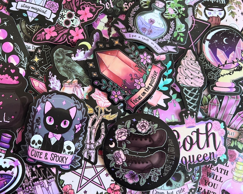 May include: A collection of colorful stickers with a gothic theme. Designs include a black cat with skulls, a crystal, a raven, a potion bottle, and the text "Cute & Spooky" and "Focus on the positive". The stickers are in shades of black, pink, purple, and white.
