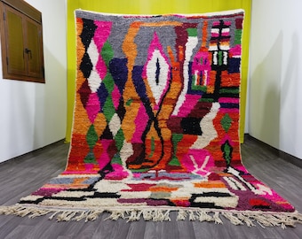May include: A colorful Moroccan rug with a geometric pattern in shades of pink, orange, green, blue, and white. The rug has a fringe border and is made of wool.