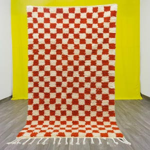 Puede incluir: Una alfombra de cuadros rojos y blancos con un borde de flecos. La alfombra está hecha de un material esponjoso y texturizado.