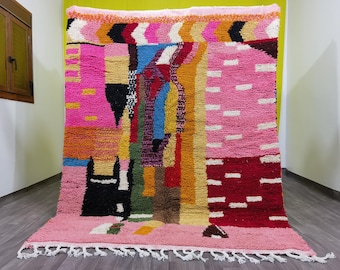 Puede incluir: Una alfombra marroquí colorida con patrones geométricos en tonos de rosa, rojo, naranja, amarillo, azul, verde y negro. La alfombra tiene un borde de flecos.