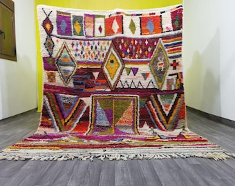 May include: A colorful Moroccan rug with a geometric pattern in shades of red, pink, blue, green, and yellow. The rug has a white background and a fringe border.