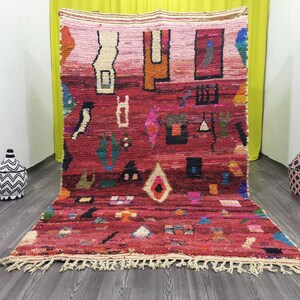 May include: A colourful Moroccan rug with a red background and geometric patterns in shades of pink, blue, green, and yellow. The rug has a fringed border.