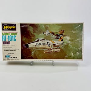 May include: A model kit box featuring a McDonnell-Douglas RF-101C Voodoo aircraft. The box art shows a silver and black jet with U.S. Air Force markings, and another aircraft in the background. The box includes the Hasegawa and Min-Craft logos.