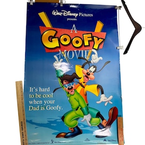 May include: A Goofy Movie poster featuring Goofy and his son, Max, in vibrant colors. The poster has a blue background with the movie title in large, colorful letters. The text "It's hard to be cool when your Dad is Goofy" is also visible.