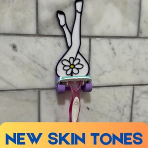 May include: A purple 3D printed razor holder shaped like a woman's legs with a daisy in the center. A pink razor is in the holder.