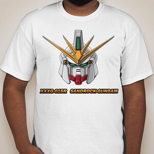 Puede incluir: Camiseta blanca con una ilustraci&oacute;n detallada de una cabeza de robot Gundam. La cabeza del robot es principalmente blanca, con detalles dorados, rojos y verdes. El texto "XXXG-01SR SANDROCK GUNDAM" est&aacute; impreso debajo en dorado.