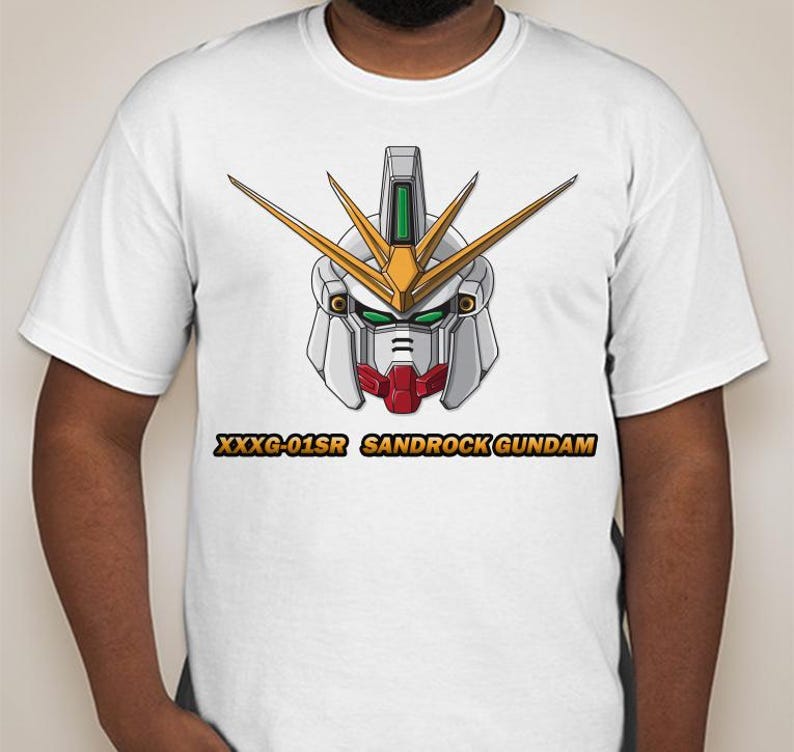 Puede incluir: Camiseta blanca con una ilustraci&oacute;n detallada de una cabeza de robot Gundam. La cabeza del robot es principalmente blanca, con detalles dorados, rojos y verdes. El texto "XXXG-01SR SANDROCK GUNDAM" est&aacute; impreso debajo en dorado.