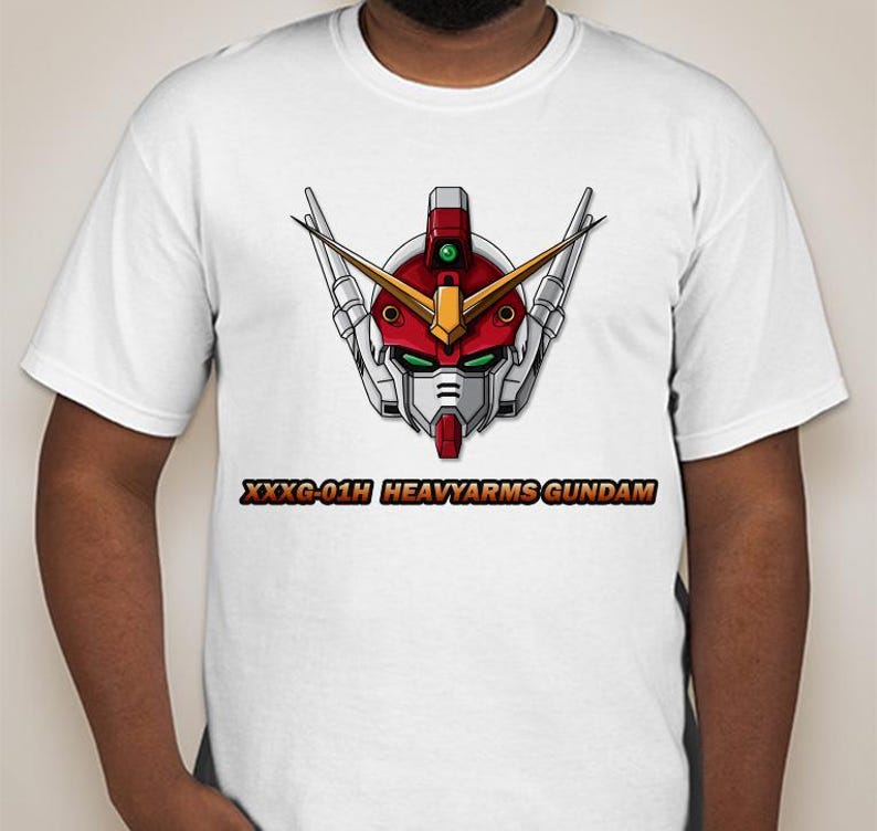 Pu&ograve; includere: Maglietta bianca con un'immagine di una testa di robot rosso, bianco e verde e il testo "XXXG-01H HEAVYARMS GUNDAM".