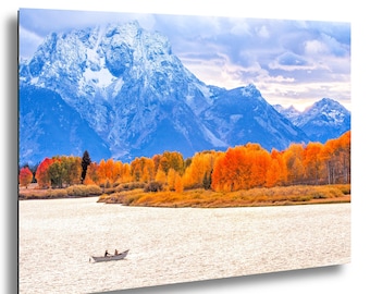 Puede incluir: Impresión de un paisaje con una cordillera nevada bajo un cielo nublado. En primer plano, un lago con un pequeño bote, y en el medio, árboles otoñales de colores vibrantes. La obra está montada en un marco negro.