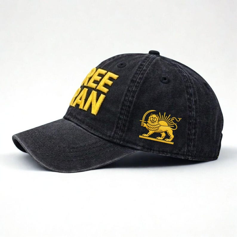 Puede incluir: Gorra de b&eacute;isbol negra con las palabras "FREE IRAN" bordadas en letras amarillas. Un emblema amarillo de le&oacute;n y sol est&aacute; en el lateral. La gorra tiene una visera curva y un aspecto desgastado.