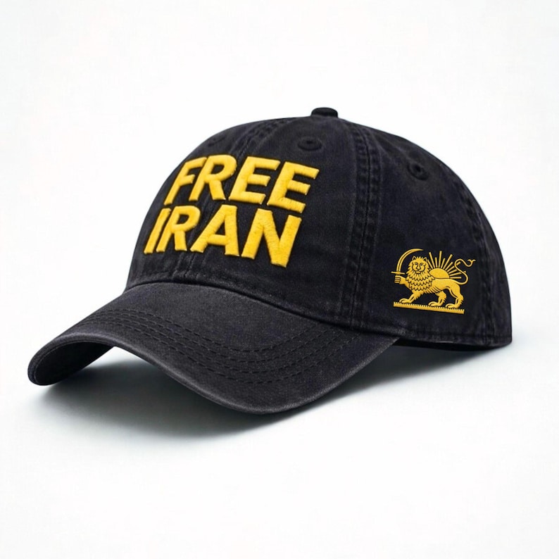 Puede incluir: Gorra de b&eacute;isbol negra con la inscripci&oacute;n "FREE IRAN" bordada en amarillo. Un emblema dorado de un le&oacute;n y un sol est&aacute; presente en el lateral. La tela es oscura y texturizada.