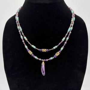 May include: A two-strand necklace with purple and turquoise beads and a gold pendant with a purple amethyst stone.