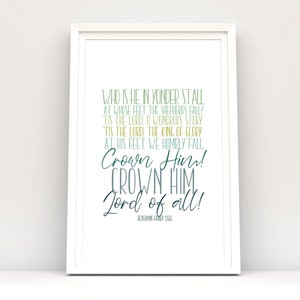 Puede incluir: Una impresión enmarcada con el texto "WHO IS HE IN YONDER STALL...Crown Him! Lord of all!" en verde y verde azulado oscuro. El marco blanco se encuentra en un estante blanco contra una pared blanca. La impresión es un artículo decorativo.