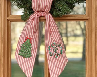 May include: A red and white striped fabric ribbon tied in a knot, featuring an embroidered green Christmas tree with a red bow on one tail and a green wreath with a red berry border and the letter P in the center on the other tail.