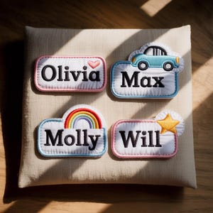 May include: Four embroidered name patches on a beige background. The patches are rectangular with rounded edges and feature the names "Olivia", "Max", "Molly", and "Will". Each patch has a unique design element, including a heart, car, rainbow, and star.