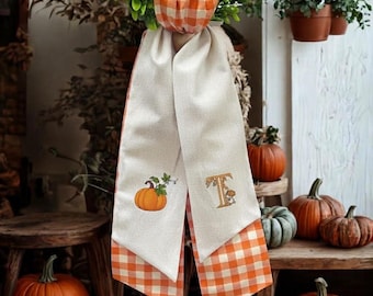 Può includere: Uno stendardo decorativo in tessuto da appendere con un motivo a quadretti arancione e bianco sul retro e un davanti color crema. La parte anteriore presenta una zucca arancione ricamata e la lettera T decorata con piccole foglie autunnali.