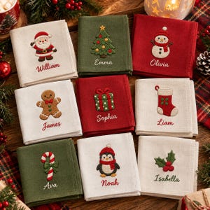 May include: A collection of eight square fabric napkins in cream, olive green, and red. Each napkin features embroidered holiday motifs including Santa, a tree, snowman, gingerbread man, gift, stocking, candy cane, penguin, and holly with names.