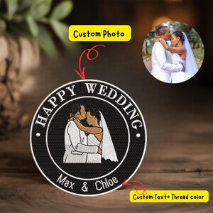 以下が含まれることがあります： 「HAPPY WEDDING」の文字が刺繍されたパッチ。中央には抱き合うカップルの画像があります。パッチには「Max & Chloe」の名前とカップルの小さな写真が含まれています。パッチは黒色で、白とタン色の刺繍が施されています。