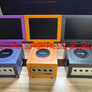 May include: Three retro game consoles in blue, orange, and black, each with a matching screen. The screens are framed in purple, orange, and black. The text "LCD CANNOT SUPPORT PAL SYSTEM CONSOLE" is displayed across the top of the consoles.