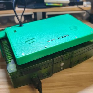 Może przedstawiać: Zielone prostokątne urządzenie elektroniczne z pasującą zieloną g&oacute;rną pokrywą. G&oacute;rna pokrywa ma szereg małych śrub i rząd tekstu. Urządzenie znajduje się na ciemniejszym zielonym urządzeniu elektronicznym.