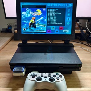 Peut inclure: Une console PlayStation 2 noire avec un écran affichant Final Fantasy X. Une manette blanche est placée devant la console. Une carte mémoire est insérée. Le texte à l'écran est en chinois.