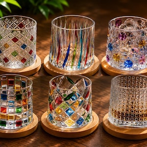 May include: Six decorative crystal drinking glasses with various colorful designs, including geometric patterns and vertical stripes. Each glass sits on a round wooden coaster. The glasses are clear, and the designs incorporate red, blue, green, and yellow.
