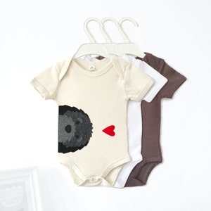 May include: Three baby onesies, one with a black and gray dog graphic and a red heart, one white, and one brown.