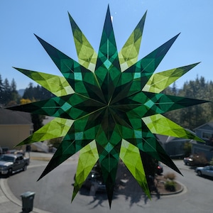 May include: A multi-pointed star ornament crafted from translucent paper in varying shades of green and lime. The geometric design features overlapping triangular segments that create a complex, layered pattern when light shines through the material.