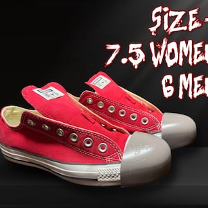 May include: Pair of red canvas trainers with white soles and toe caps. The trainers have metal eyelets and a white label on the tongue. The text on the image reads "SIZE - 7.5 WOMEN 6 MEN".