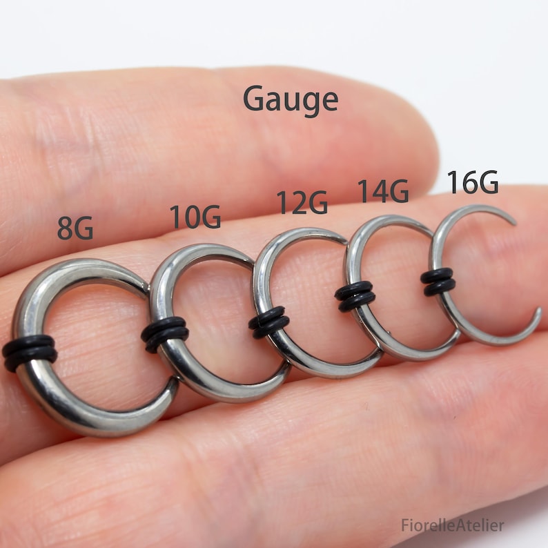Peut inclure: Gros plan sur cinq boucles d'oreilles de calibre argent&eacute;es avec des anneaux en caoutchouc noirs. Les tailles sont &eacute;tiquet&eacute;es 8G, 10G, 12G, 14G et 16G. Le mot "Gauge" est &eacute;crit au-dessus.