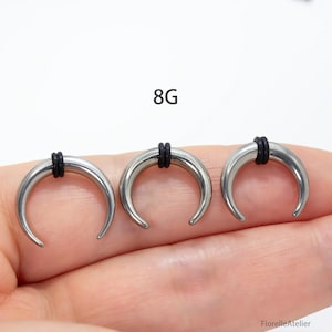 Peut inclure: Trois &eacute;carteurs d'oreille argent&eacute;s en forme de croissant avec des anneaux en caoutchouc noirs. Le texte "8G" est affich&eacute; au-dessus des &eacute;carteurs. Ces &eacute;carteurs sont con&ccedil;us pour les piercings d'oreille &eacute;tir&eacute;s.
