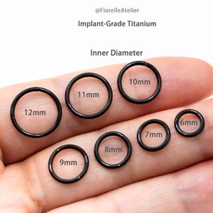 May include: Black implant-grade titanium body jewelry rings in various sizes, ranging from 6mm to 12mm inner diameter. The rings are displayed on a hand, with the sizes clearly labeled. The text "Inner Diameter" is also visible.