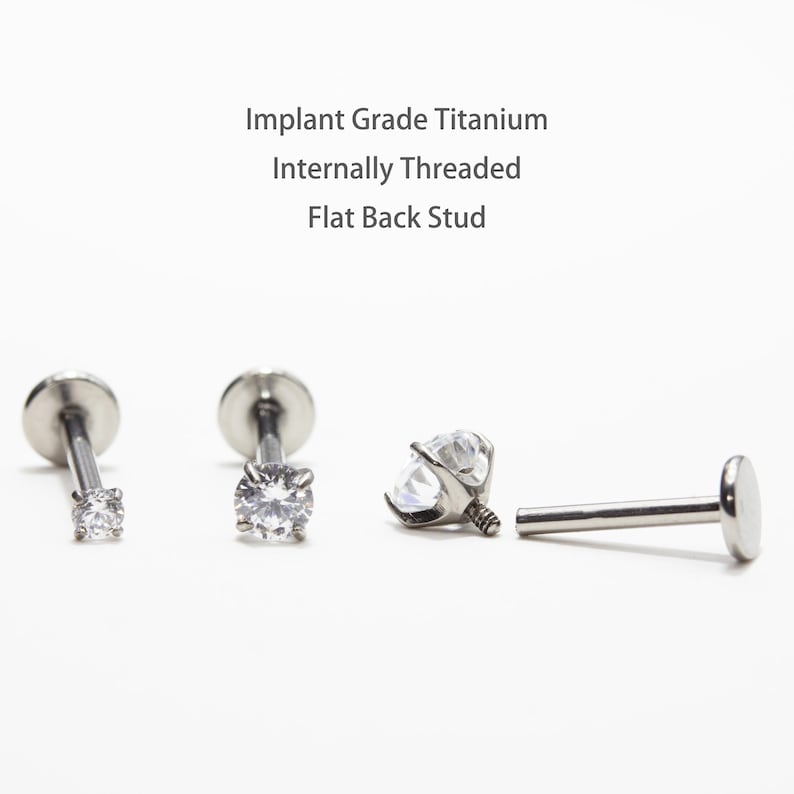 May include: Four silver-colored, flat-back stud earrings with clear, round gemstones. The studs are made of implant-grade titanium and are internally threaded. Text in the image reads: Implant Grade Titanium, Internally Threaded, Flat Back Stud.