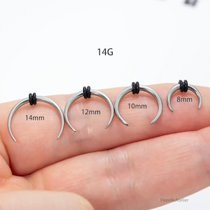 Peut inclure: Quatre bijoux de corps argent&eacute;s en forme de fer &agrave; cheval avec des anneaux en caoutchouc noirs. Les tailles sont de 14 mm, 12 mm, 10 mm et 8 mm. Le texte "14G" est au-dessus des bijoux.
