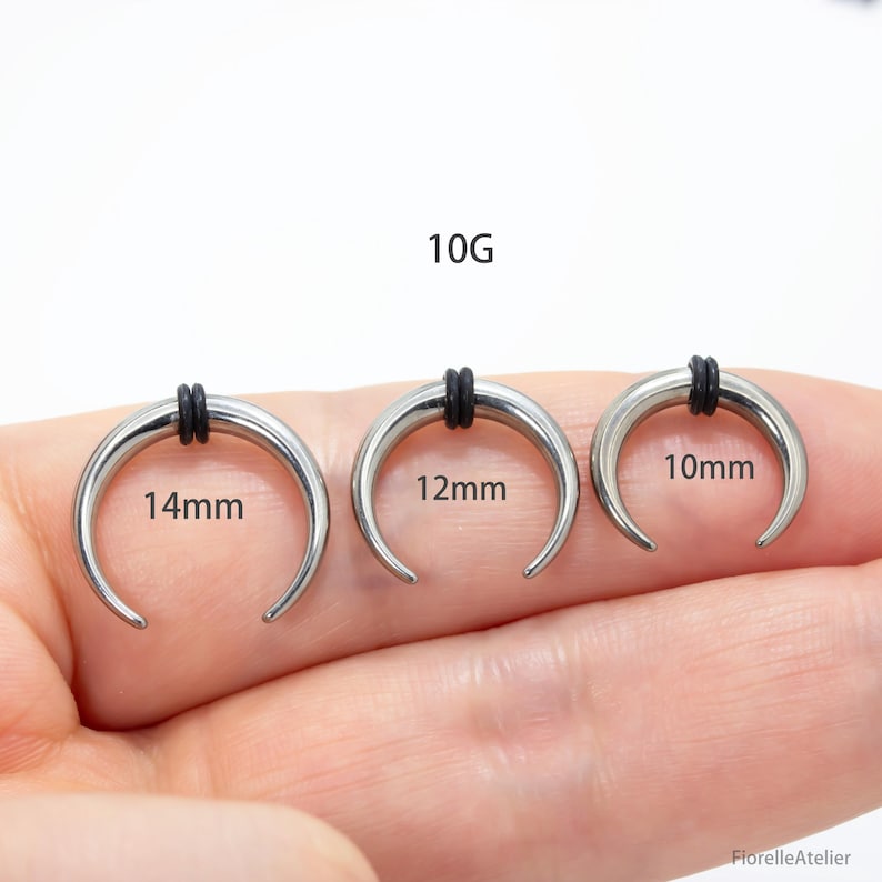 Peut inclure: Trois &eacute;carteurs d'oreille argent&eacute;s en forme de croissant avec des bandes de caoutchouc noires. Les jauges sont &eacute;tiquet&eacute;es avec les tailles : 14 mm, 12 mm et 10 mm. Le texte "10G" est &eacute;galement pr&eacute;sent. Ce sont des bijoux de corps.